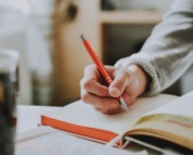 person holding on red pen while writing on book